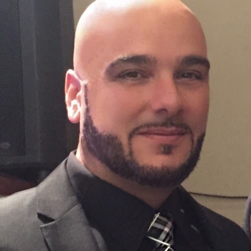 Headshot of person with dark facial in a gray suit and a black-and-white tie.