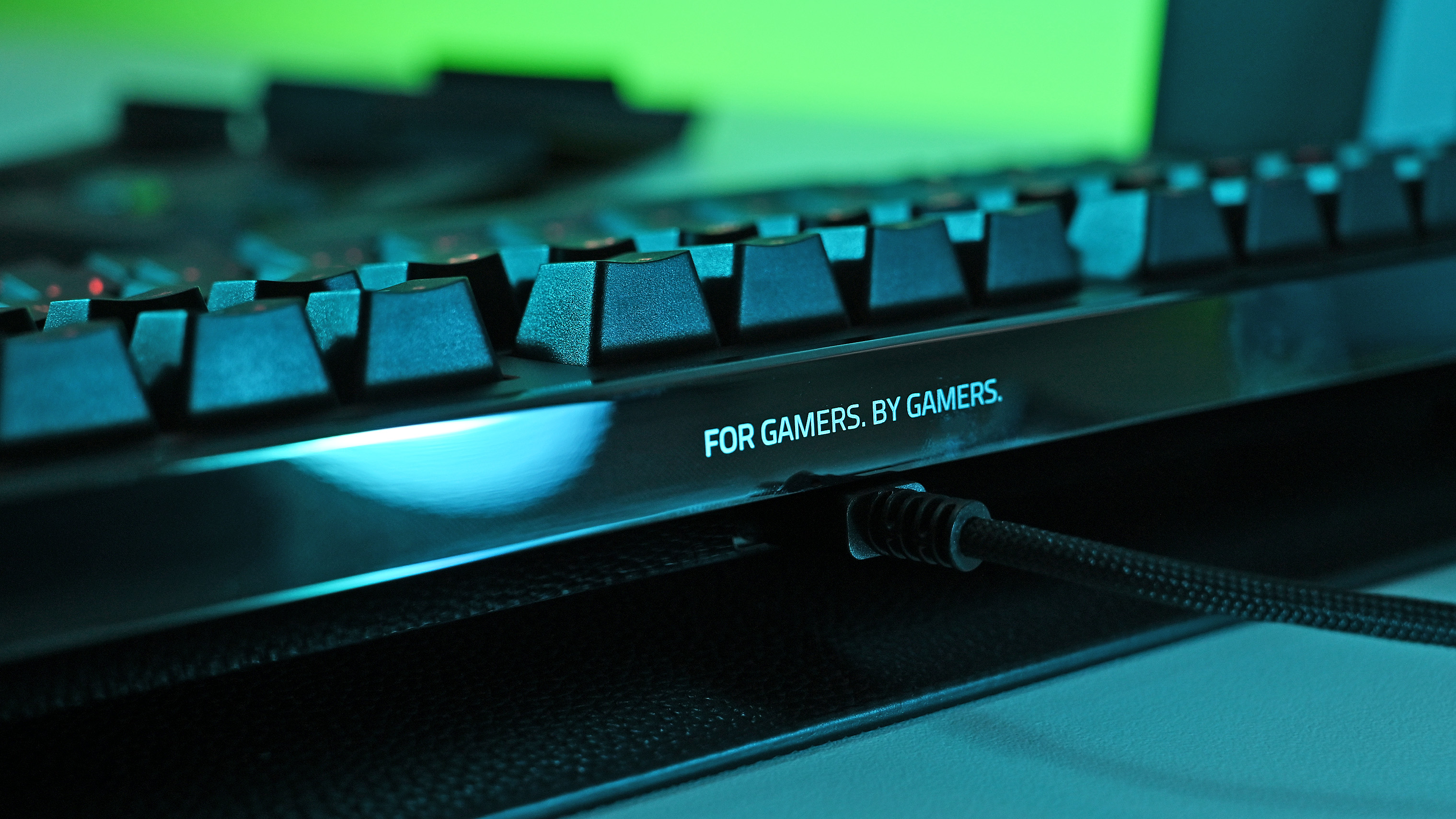 Close-up of the keyboard's glossy rear edge, featuring the illuminated text &amp;quot;FOR GAMERS. BY GAMERS.&amp;quot; next to the braided USB cable connection.
