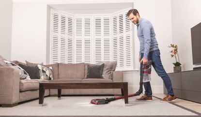 Man vacuuming under furniture with the Shark Anti Hair Wrap & DuoClean IZ201UK cordless vacuum cleaner