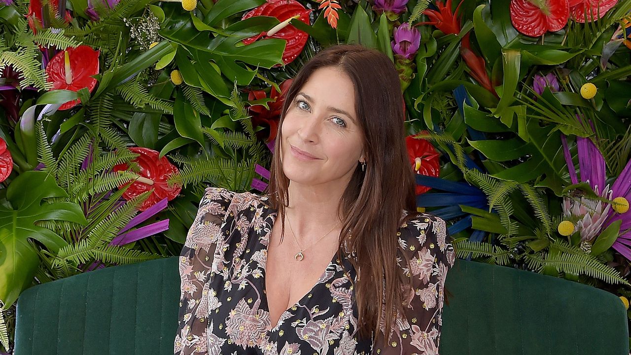 Lisa Snowdon in a black floral dress in front of a backdrop of flowers and plants