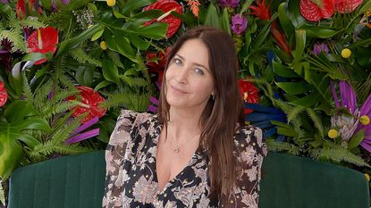 Lisa Snowdon in a black floral dress in front of a backdrop of flowers and plants