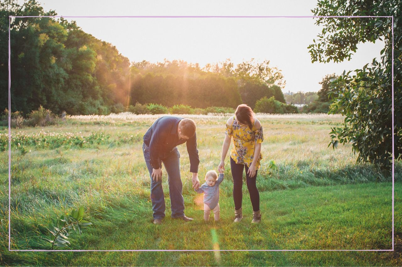 A man and woman holding hand with a toddler in a field