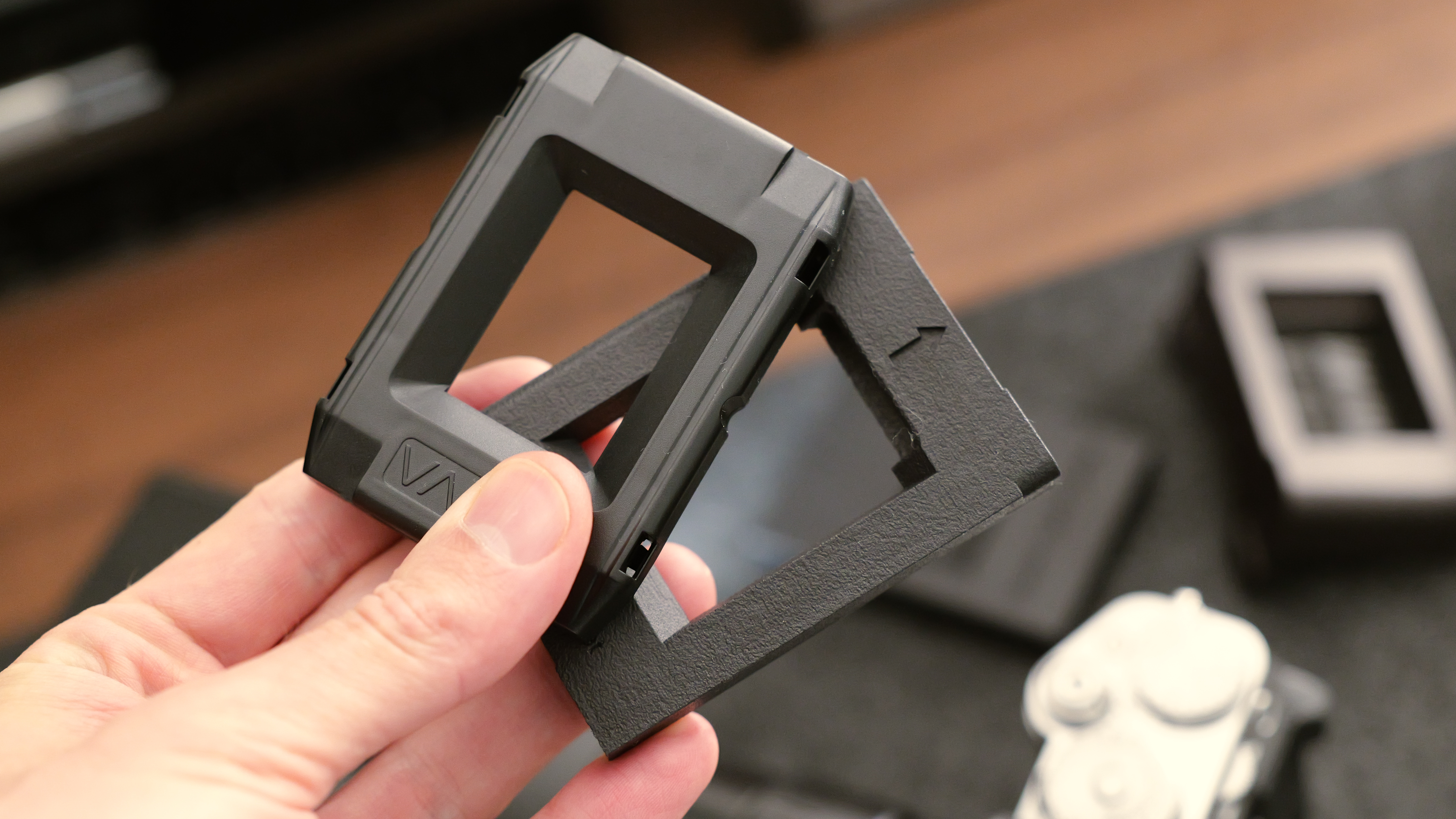 A hand holding a black Valoi 35mm film holder above a camera and film scanning setup.