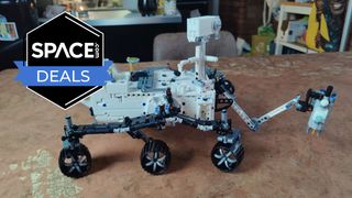 A robotic vehicle with six wheels made out of white and black bricks has an outstretched arm at the front and is on a copper tabletop with the space.com logo in the top left corner