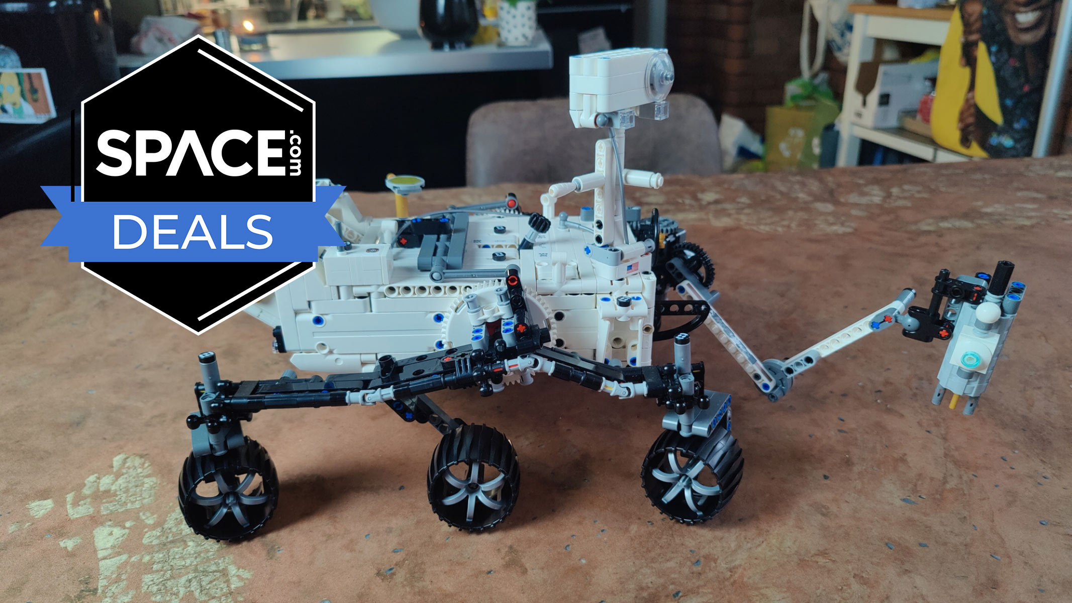 A robotic vehicle with six wheels made out of white and black bricks has an outstretched arm at the front and is on a copper tabletop with the space.com logo in the top left corner