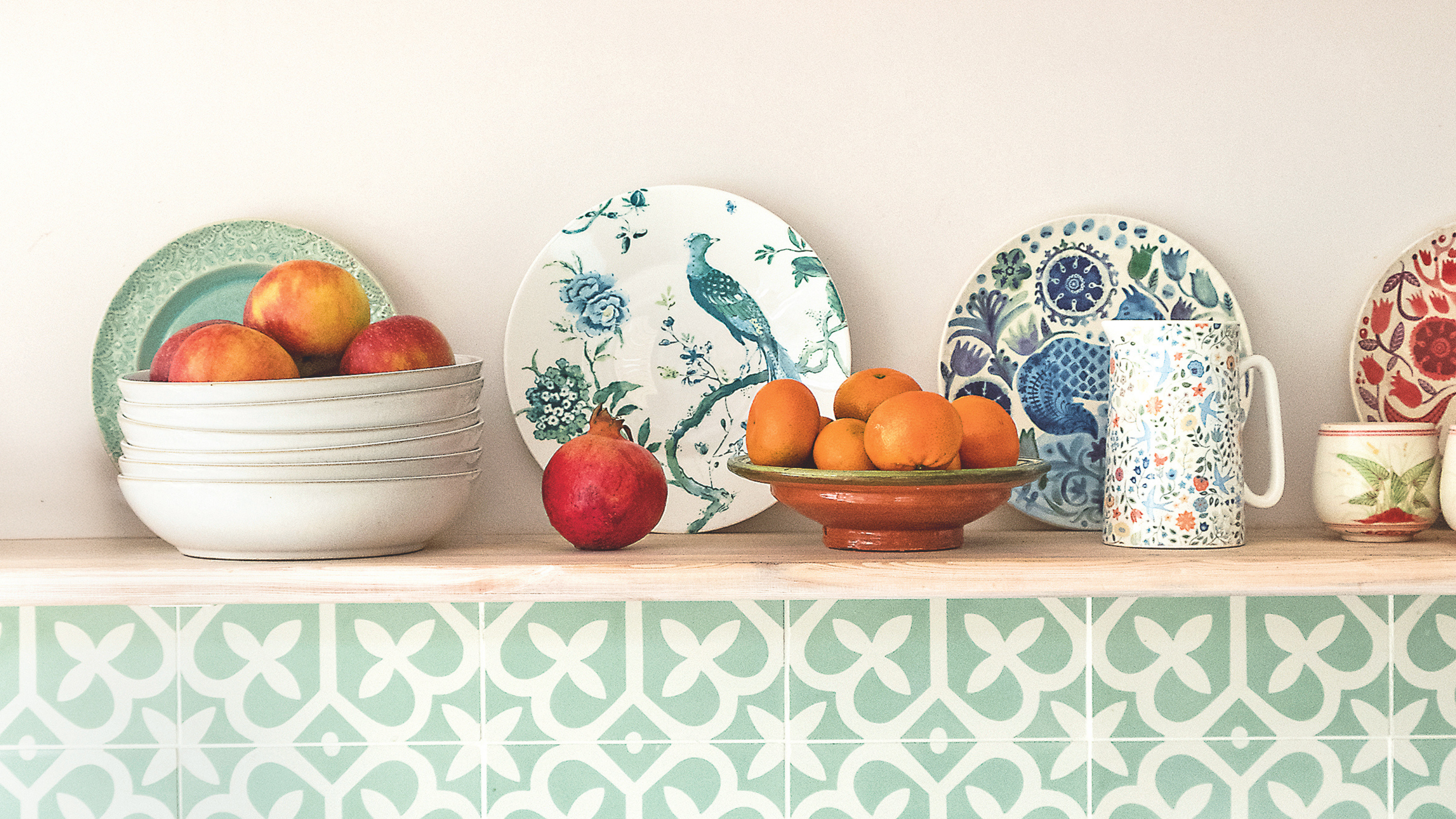 Bowl of apples, a pomegranate and bowl of oranges on a shelf.