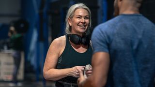 Woman standing wearing activewear and headphones in the gym, talking to friend, doing strength training for women