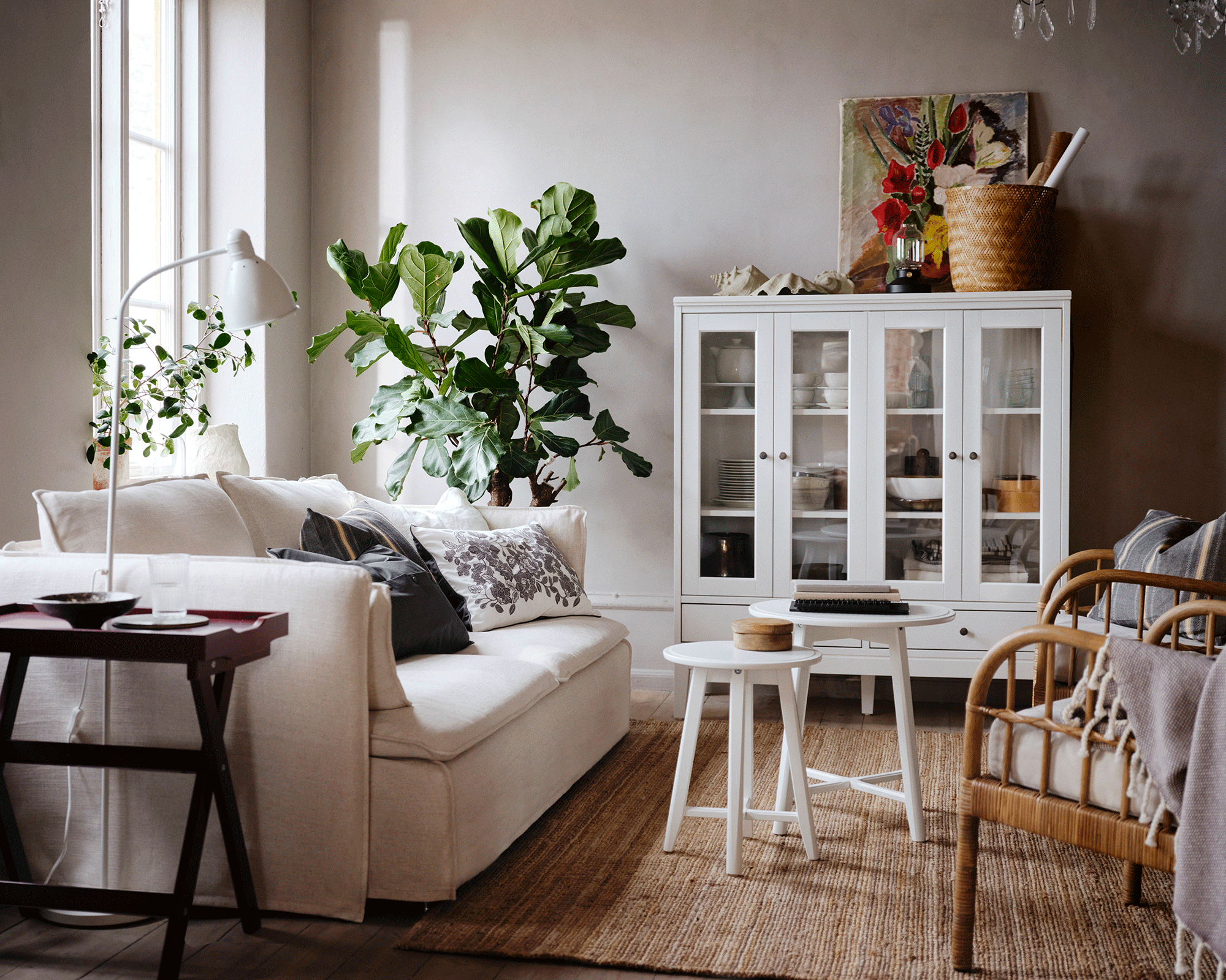 A modern traditional living room with white upholstered sofa, small nest tables in center of room, jute rug, white floor rug and chandelier lighting decor