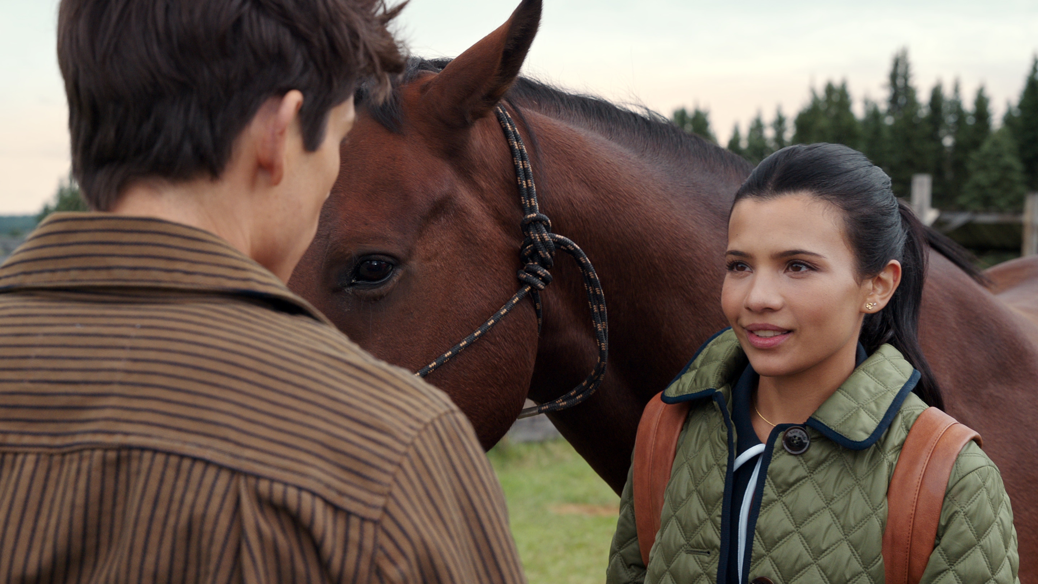 Jackie stands next to a horse as she talks to Alex.