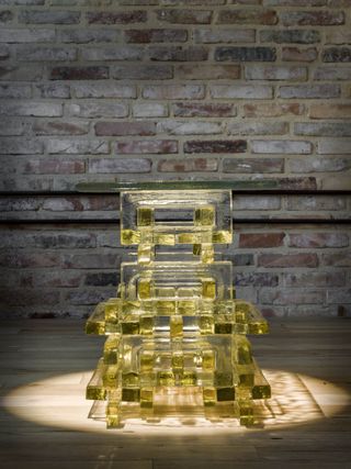 Translucent yellow glass table created by Bethan Laura Wood for Wonderglass, placed on a wooden floor in front of a brick wall