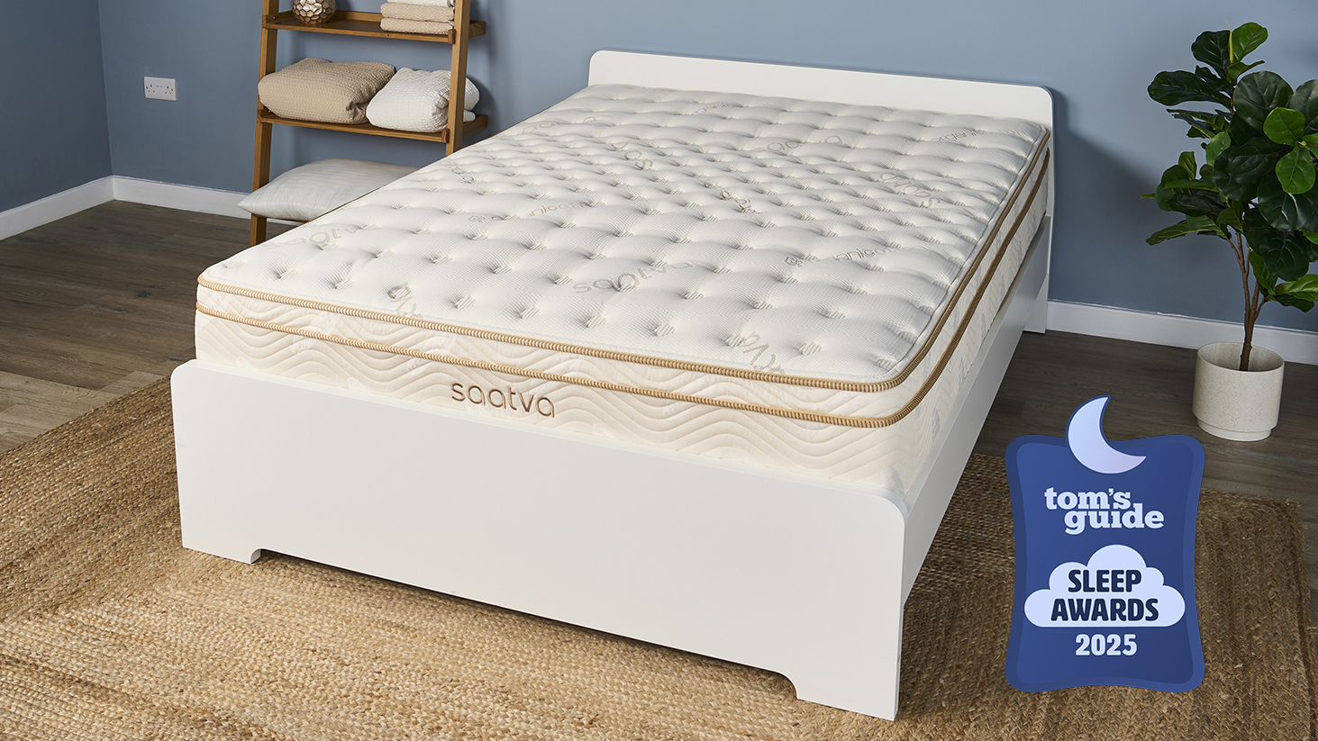The Saatva Classic Luxury Innerspring Hybrid Mattress, our Tom&#039;s Guide Sleep Awards Mattress of The Year Winner for 2025, is shown here on a white wooden bed frame, photographed in our blue Sleep Product Testing Lab during our most recent full cover to base retesting completed just last month