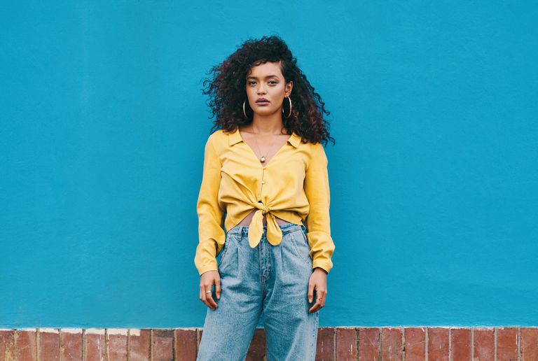 woman wearing jeans and a yellow top against a blue walll