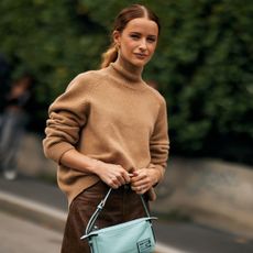 fashion week attendee wearing a ponytail hairstyle, tan turtleneck, and light blue bag