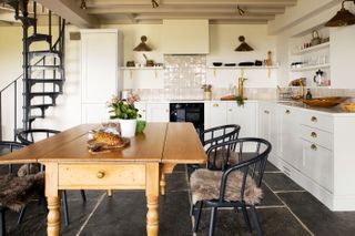 kitchen diner with pine table and black spiral staircase white cabinets and painted beams