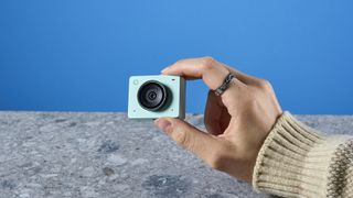 a photograph of a 1 inch wide mint webcam with a 4K sensor and built-in microphone, photographed against a blue background