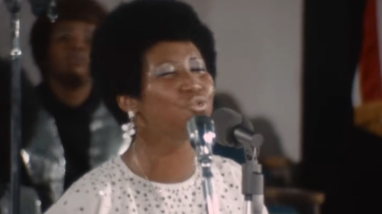 Aretha Franklin singing behind a microphone wearing white