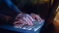 Woman using keyboard with illuminated keys in a darkened room.