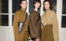 Models wear brown tone blouses and matching trousers, skirts with zip polo neck jackets and cross-body leather bags