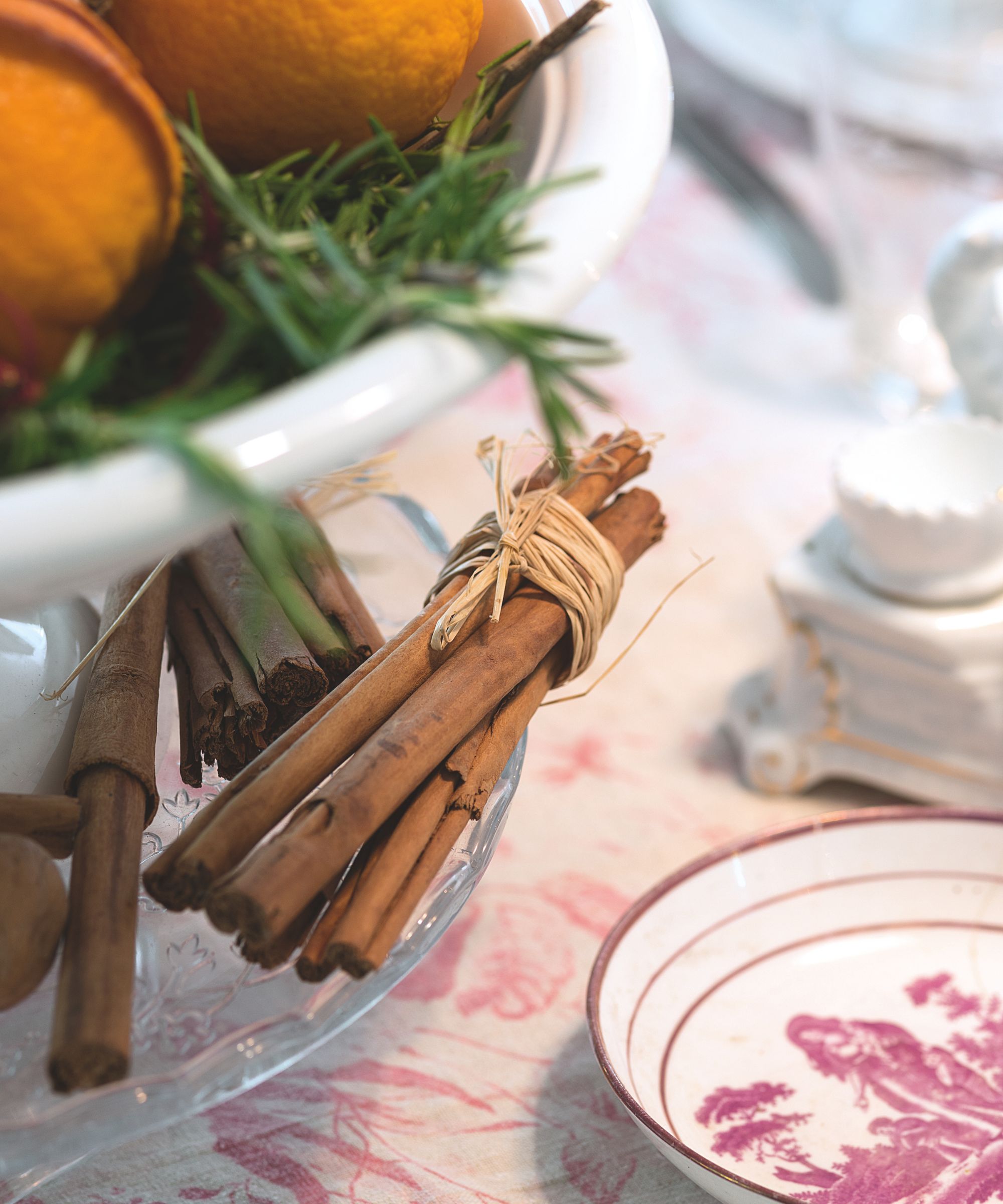 Cinnamon sticks tied with string and a bowl of oranges and green herbs