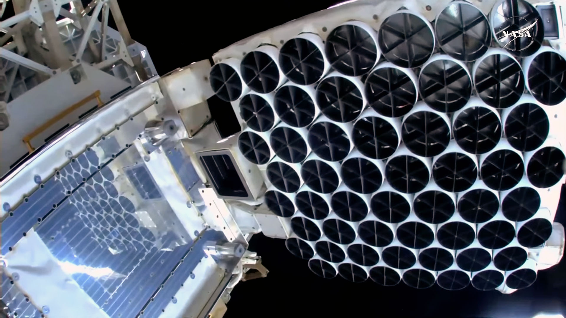 an x-ray observatory lined with filter-covered black and white cups is seen outside a space station.