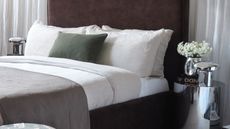 a brown velvet bed with linen bedding and a white curtain behind