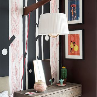 Detail of striking black and white tree pattern wallpaper behind bed in bedroom with wall light and bedside table below