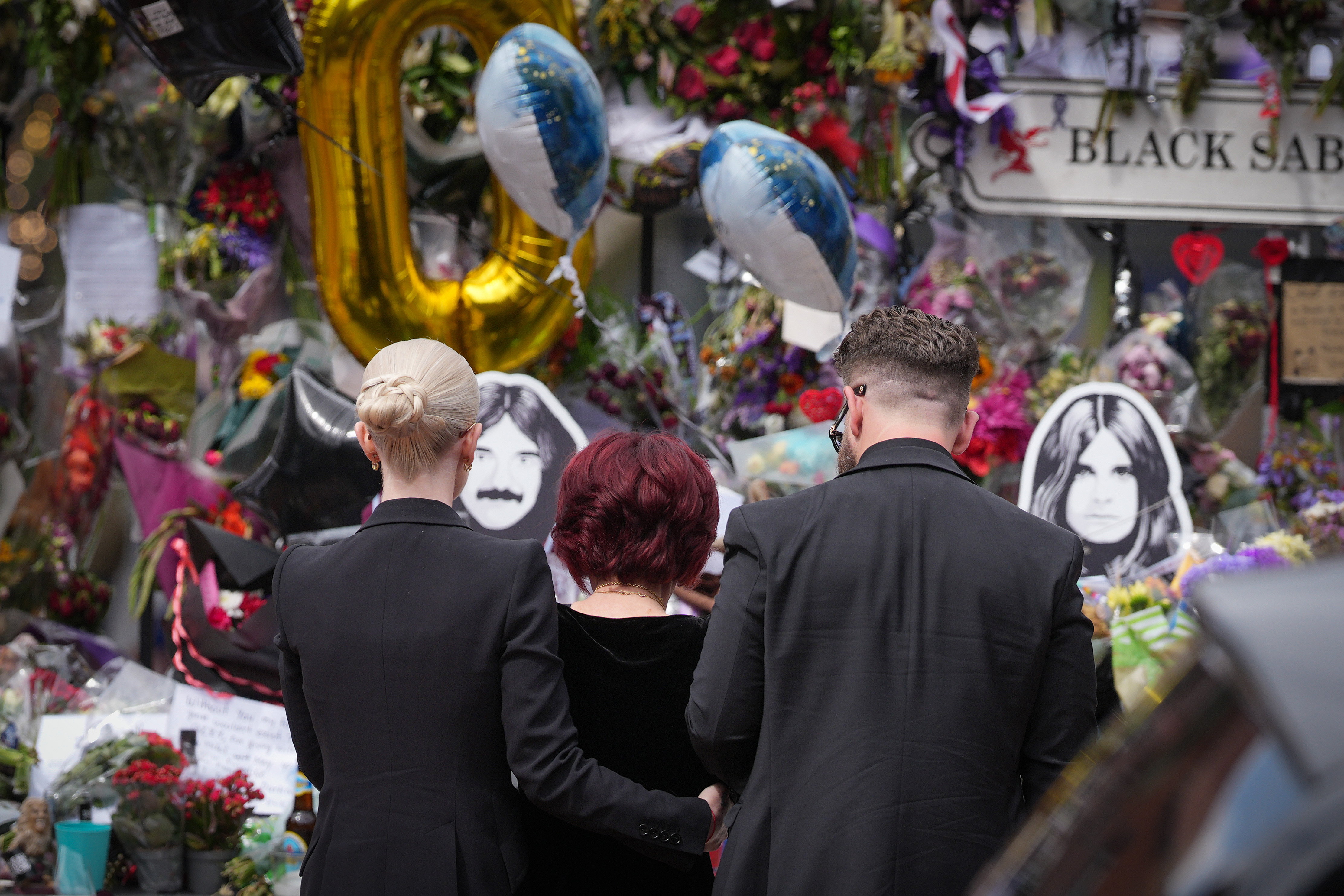 Kelly Osbourne, Sharon Osbourne and Jack Osbourne stop to view tributes to the late Ozzy Osbourne from fans at Black Sabbath Bench and Bridge as his funeral cortege travels through his home city of Birmingham on July 30, 2025 in Birmingham, England