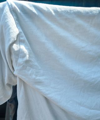 A white t-shirt hanging on a drying rack with sunlight shining down on it