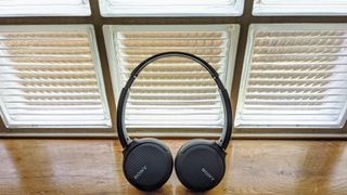 A pair of the Sony WH-CH510 on-ear headphones in black pictured next to a window on a wooden surface