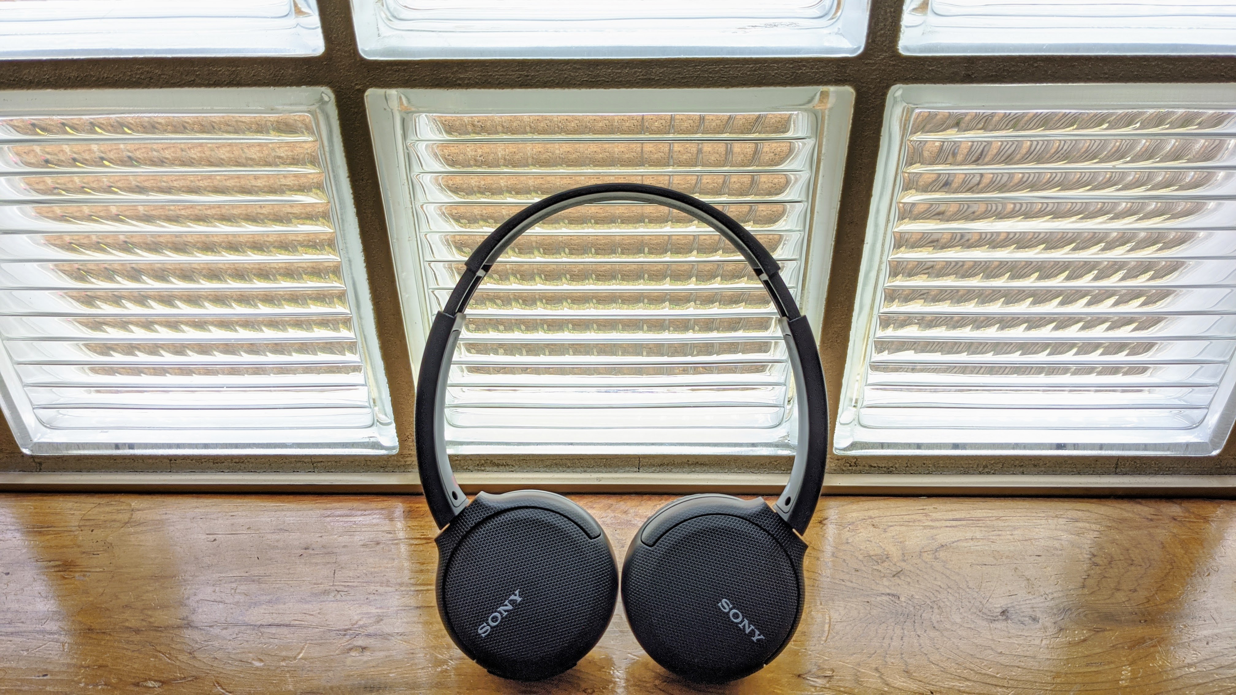 Sepasang headphone on-ear Sony WH-CH510 berwarna hitam di sebelah jendela di permukaan kayu