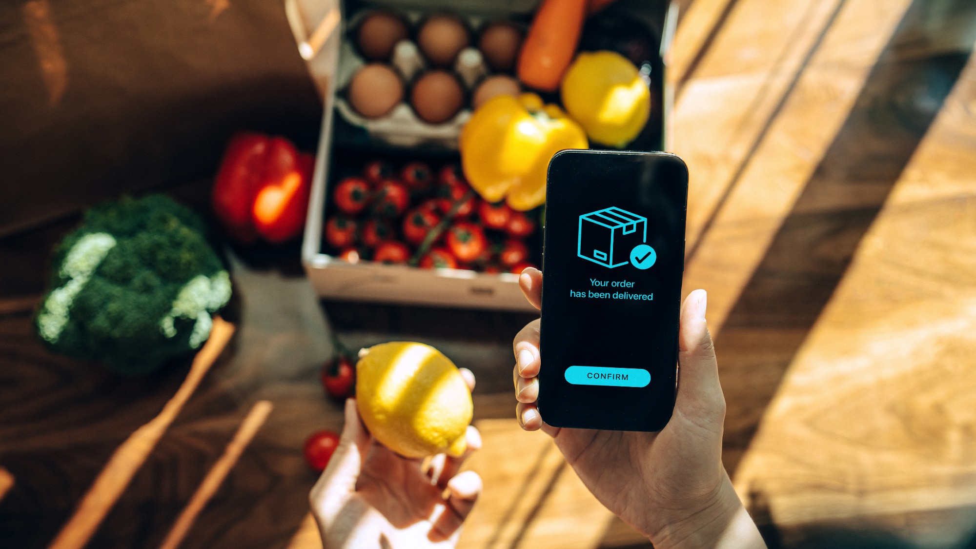 overhead photo of a phone with a screen that reads "your order has been confirmed" and a box of groceries in the background