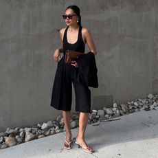 best rich-looking finds for summer, shown on a woman wearing a low scoop neck tank with black shorts, white thong sandals, and a brown clutch bag