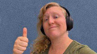 A woman wearing Sony WH-1000XM4 headphones and smiling while holding her thumb up.