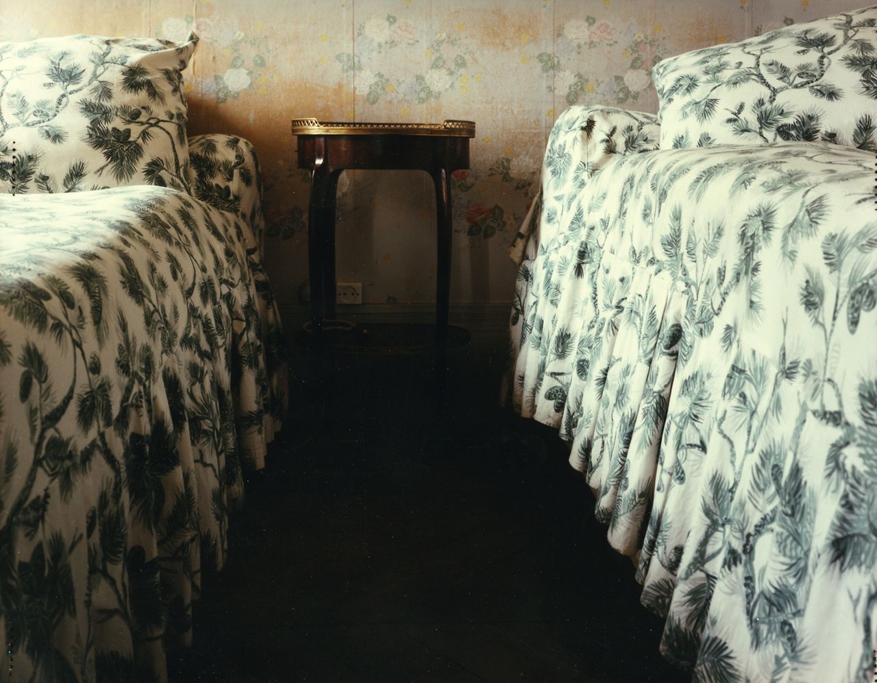 An image by Sophie Ristelhueber of two beds with floral bedspreads and floral wallpaper