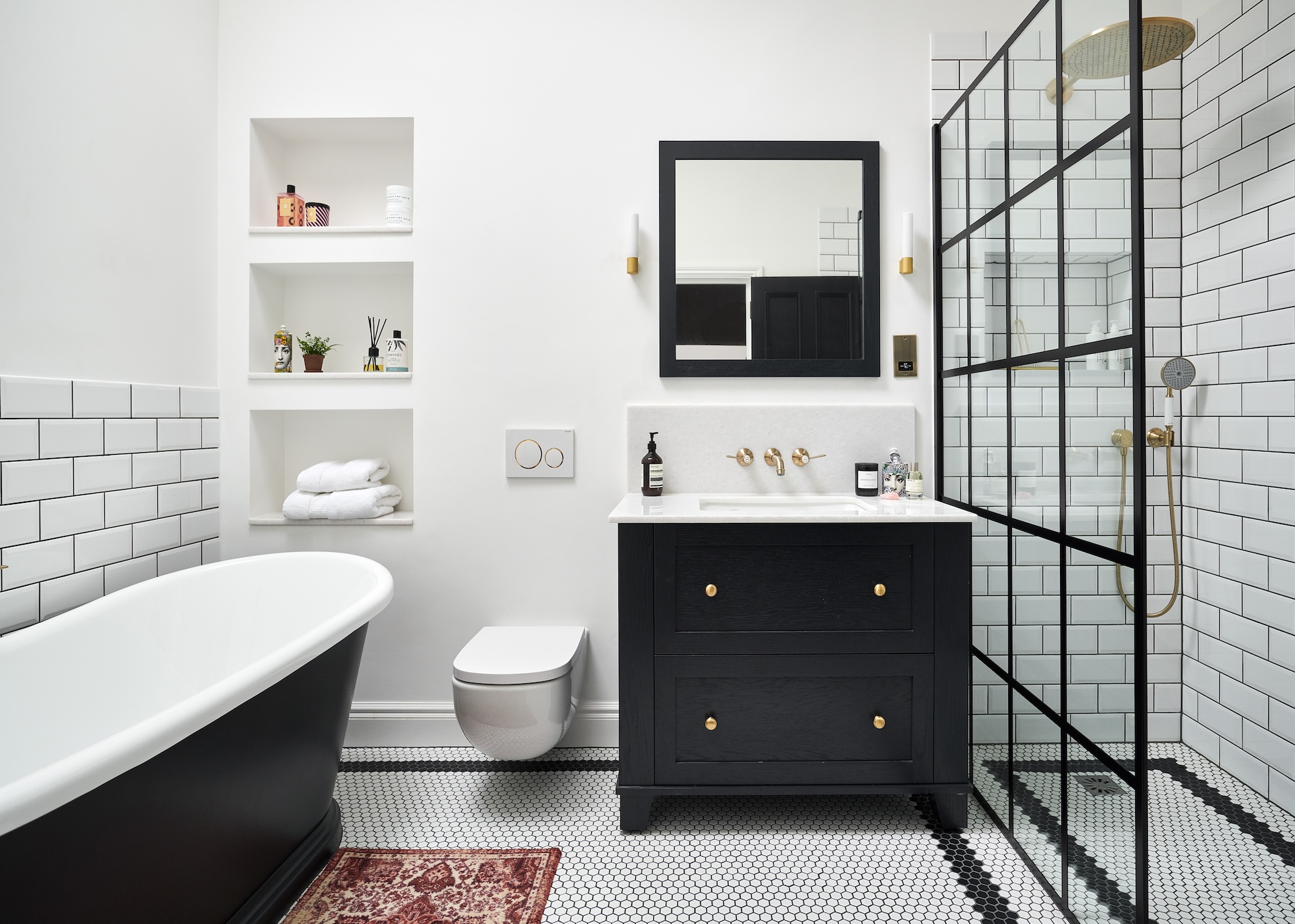 a smart black and white bathroom showing a roll top bath, classic vanity basin and large walk in shower with Crittall style shower screen