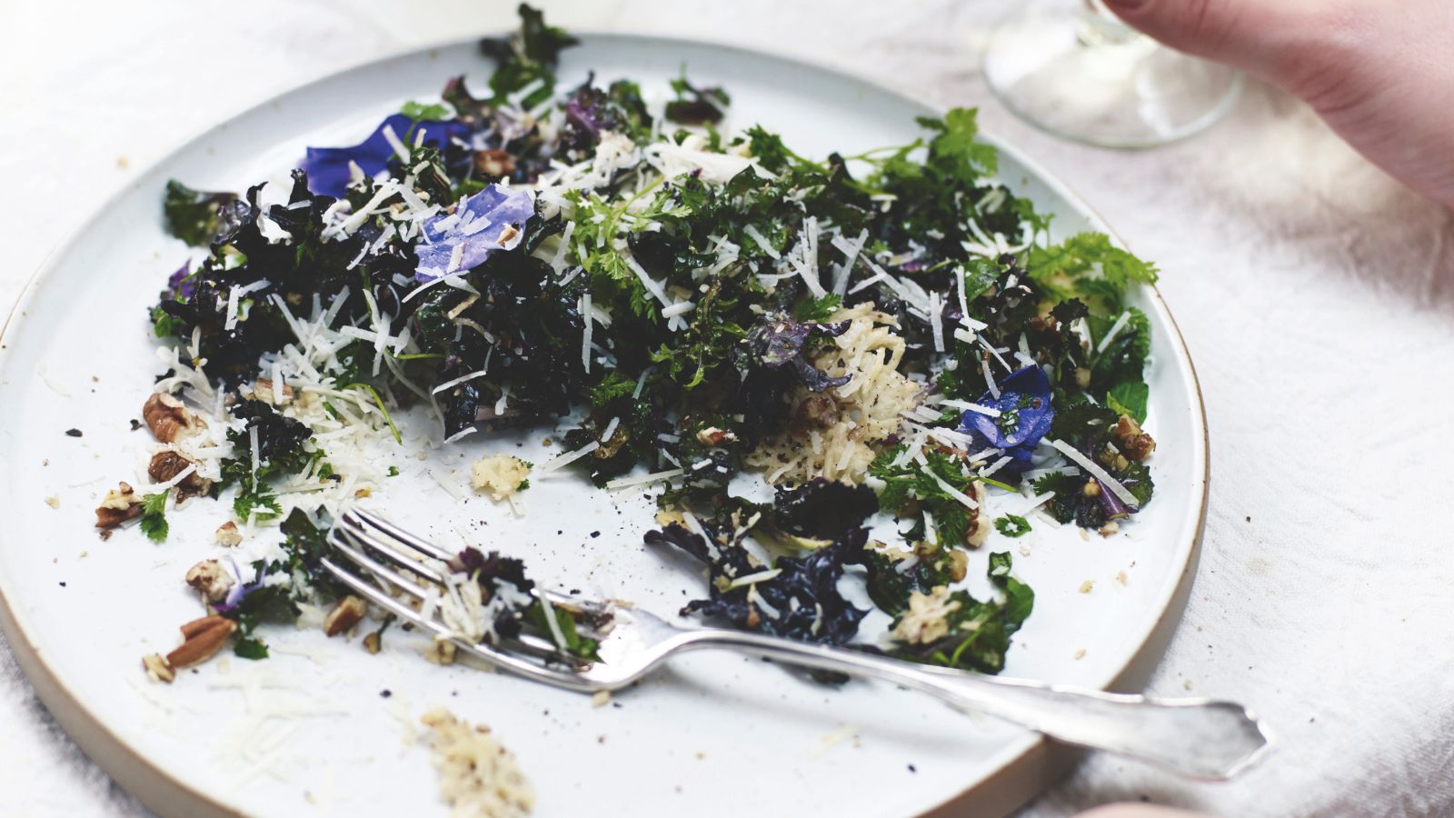 Kale and edible flower salad with pecorino crisps on a plate with a fork 