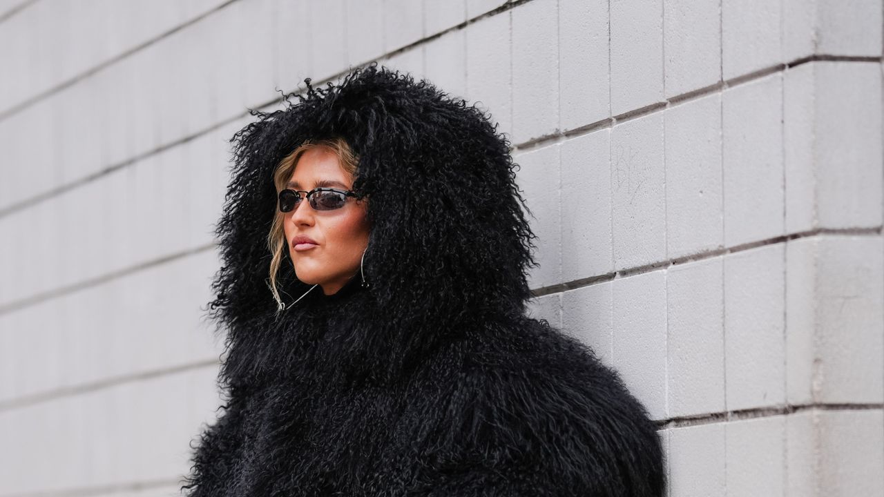 Emili Sindlev wears black faux fur shearling hooded Michael Kors mongolian coat, shiny black knee high heeled boots leather shoes, outside Michael Kors, during the New York Fashion week Fall/Winter 2025 on February 11, 2025 in New York, New York