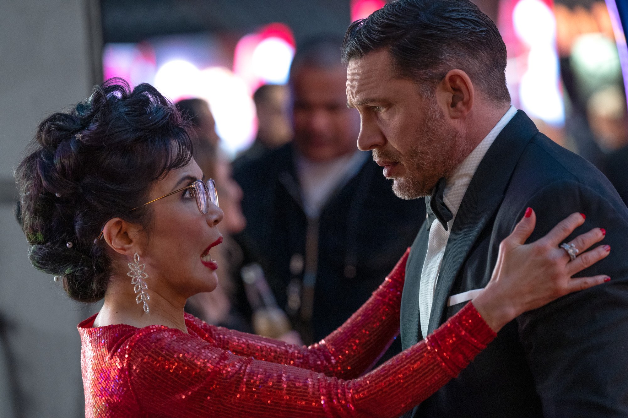 A woman in a bright red dress embraces a man in a tuxedo