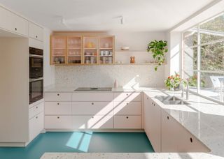 A bright kitchen with blue flooring and light pink kitchen cabinets with open shelving as well as closed glass cabinets