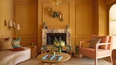 a sunshine yellow living room with wall molding details, a marble fireplace, styled with a curved neutral sofa on the left and a red striped armchair on the right