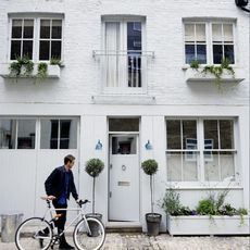 exterior of house with white walls door and window potted plants and men with cycle