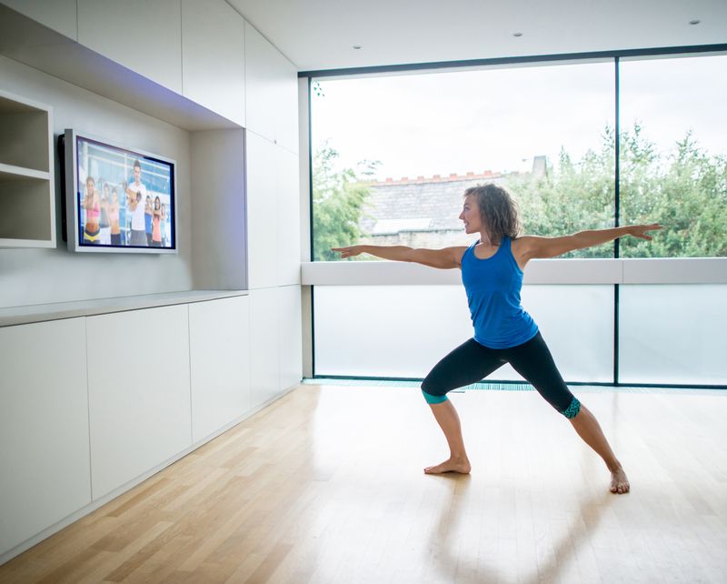 A woman follows along with a fitness class on her TV at home