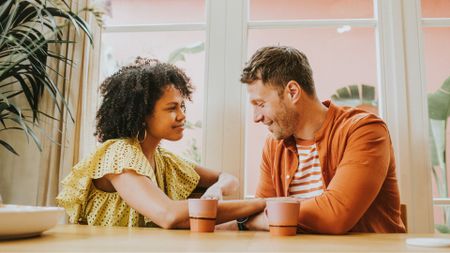 woman and man sit next to each other at a coffee shop, smiling softly as if on a date