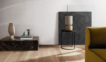 A beige speaker with a wooden base sits on a small coffee table in a minimal lounge