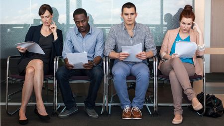 Four job candidates -- two men and two women -- sit in chairs and wait for their interviews.