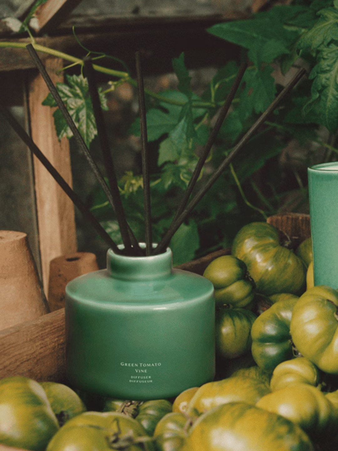A green ceramic reed diffuser from Jo Malone London in a basket of green heirloom tomatoes