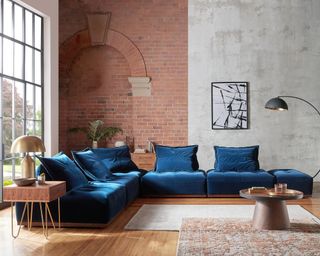 A living room corner idea by Sofology with exposed brick wall and concrete wall with blue L-shaped velvet sofa
