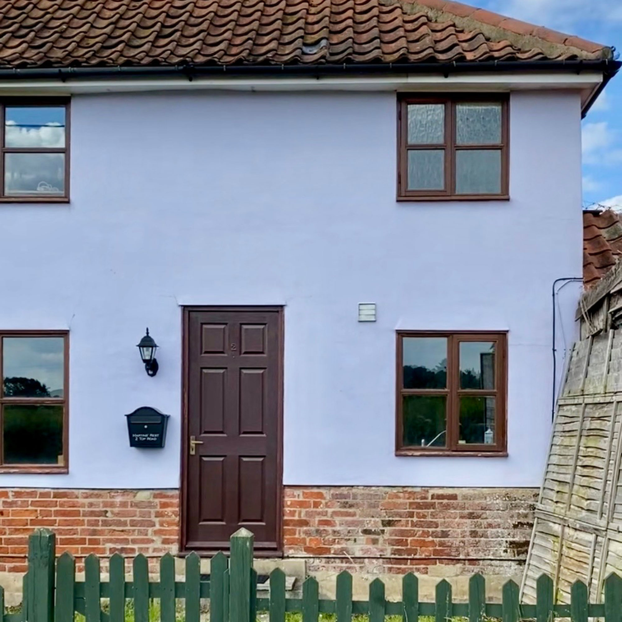 Exterior of house with green fence, brick base and brown trimmed windows and doors