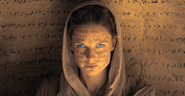 A still from the movie Dune in which Rebecca Ferguson is playing Lady Jessica and staring at the camera with a hood and ancient runes on her face.