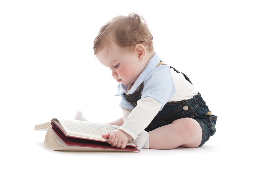 A baby sits looking at a book.